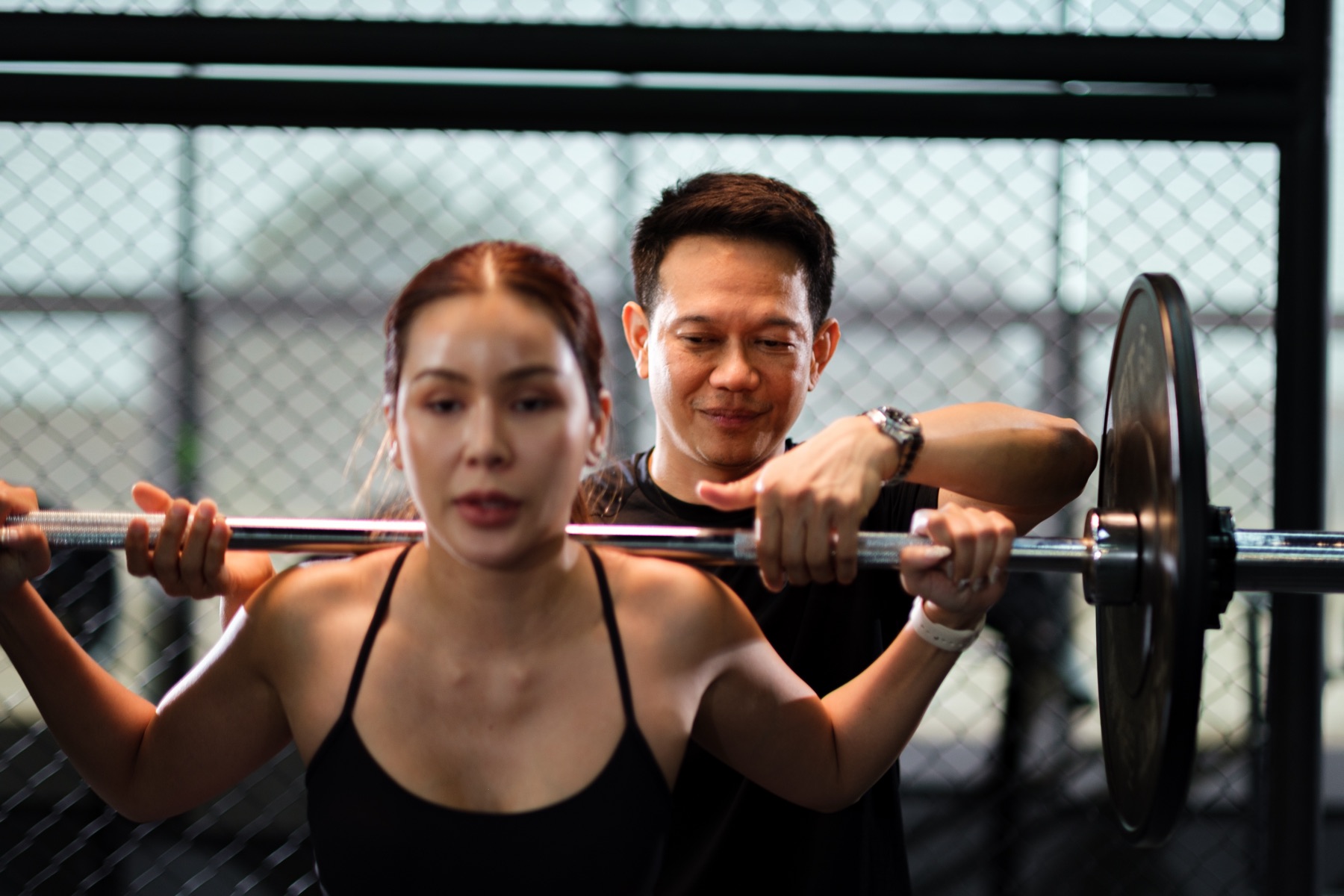 A Coach Gym coach guiding a member through a barbell lift